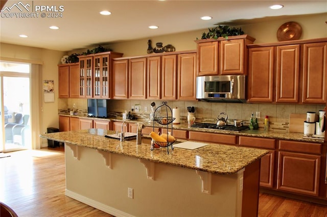 kitchen featuring a kitchen bar, stainless steel appliances, light hardwood / wood-style flooring, and an island with sink