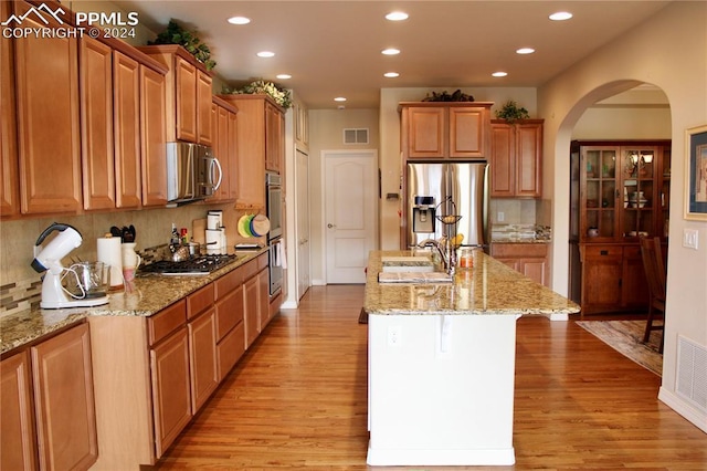 kitchen featuring tasteful backsplash, a kitchen island with sink, light stone countertops, and stainless steel appliances