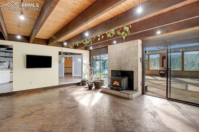 unfurnished living room featuring a wood stove, beamed ceiling, a wealth of natural light, and wood ceiling