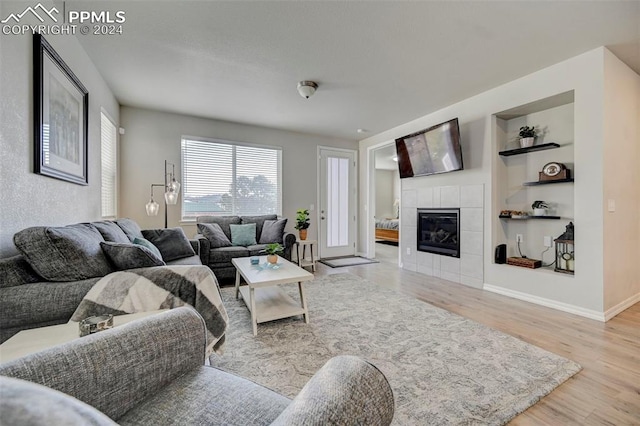 living room with light hardwood / wood-style flooring, a tiled fireplace, and built in features