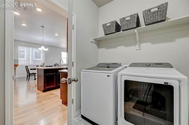 clothes washing area featuring light hardwood / wood-style flooring, washing machine and dryer, and an inviting chandelier