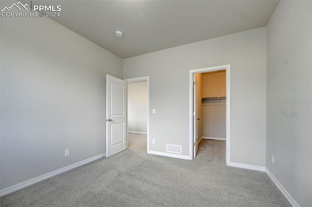 unfurnished bedroom with a spacious closet, light carpet, and a closet