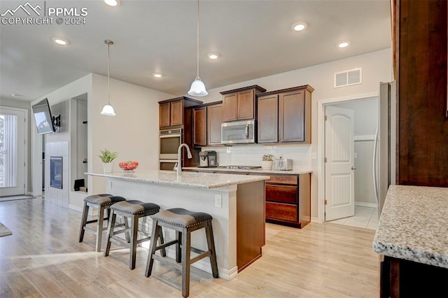 kitchen with appliances with stainless steel finishes, a kitchen island with sink, light hardwood / wood-style floors, and pendant lighting