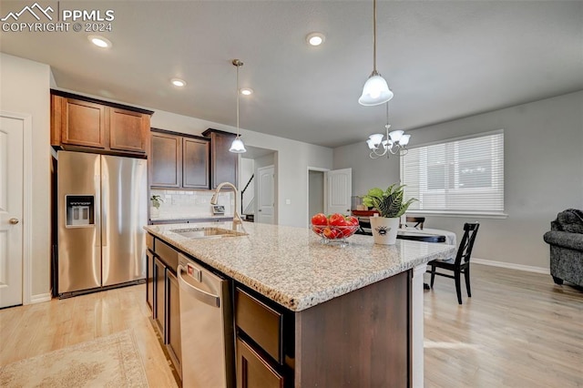 kitchen featuring a kitchen island with sink, hanging light fixtures, sink, light wood-type flooring, and appliances with stainless steel finishes