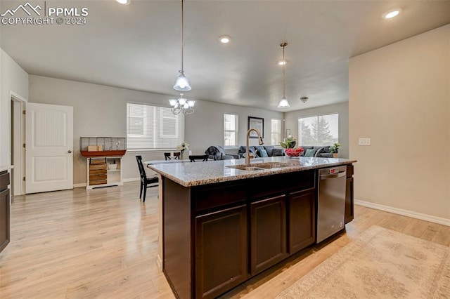 kitchen featuring sink, decorative light fixtures, light wood-type flooring, and an island with sink