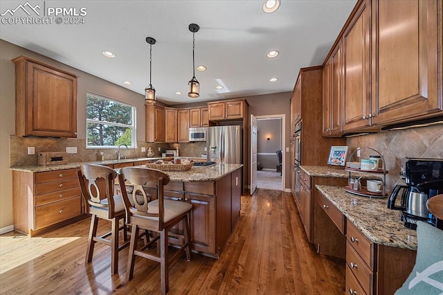 kitchen with light stone countertops, backsplash, appliances with stainless steel finishes, hardwood / wood-style flooring, and a center island