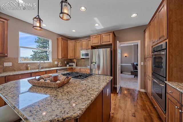 kitchen with pendant lighting, appliances with stainless steel finishes, light stone countertops, and a kitchen island