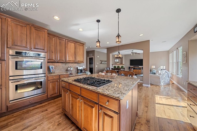 kitchen featuring light wood-type flooring, light stone counters, a center island, appliances with stainless steel finishes, and decorative light fixtures