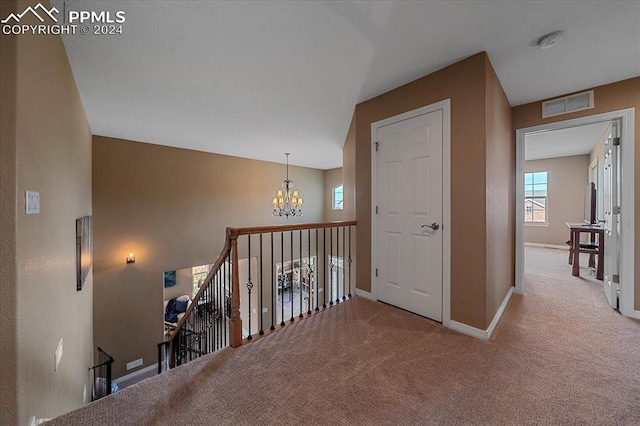 hall featuring light colored carpet and an inviting chandelier