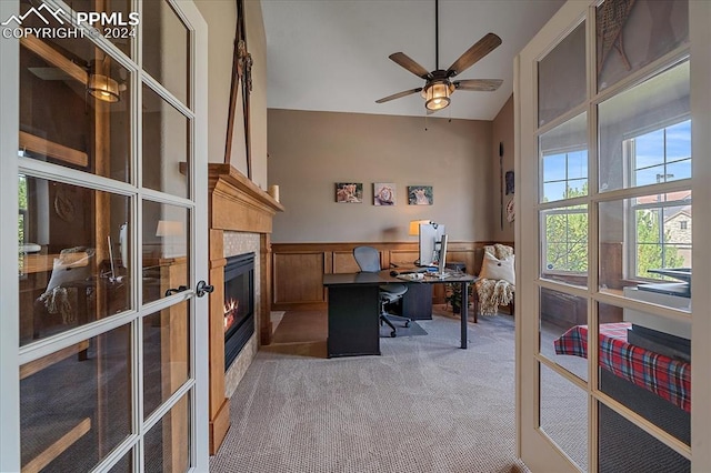 carpeted office space with ceiling fan, wooden walls, a tiled fireplace, and french doors