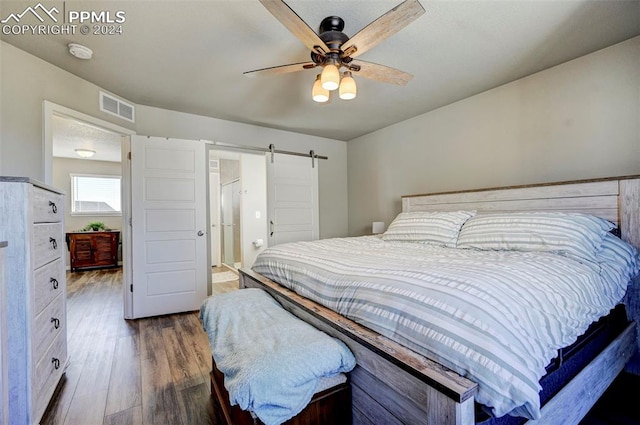 bedroom with dark hardwood / wood-style floors, a barn door, and ceiling fan