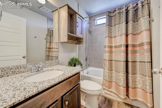 full bathroom with hardwood / wood-style flooring, toilet, shower / tub combo, vanity, and a textured ceiling