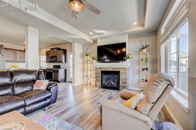 living room featuring a stone fireplace, light wood-type flooring, and ceiling fan