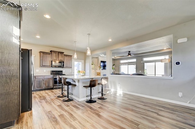 kitchen with a kitchen island, a kitchen breakfast bar, ceiling fan, light hardwood / wood-style floors, and stainless steel appliances