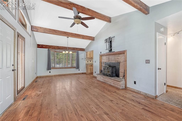 unfurnished living room with ceiling fan with notable chandelier, beamed ceiling, light hardwood / wood-style flooring, and a wood stove