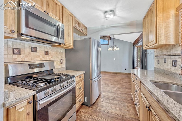 kitchen with hanging light fixtures, light hardwood / wood-style floors, appliances with stainless steel finishes, and backsplash