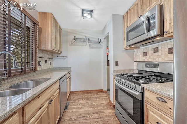 kitchen with light hardwood / wood-style floors, decorative backsplash, sink, stainless steel appliances, and light stone countertops