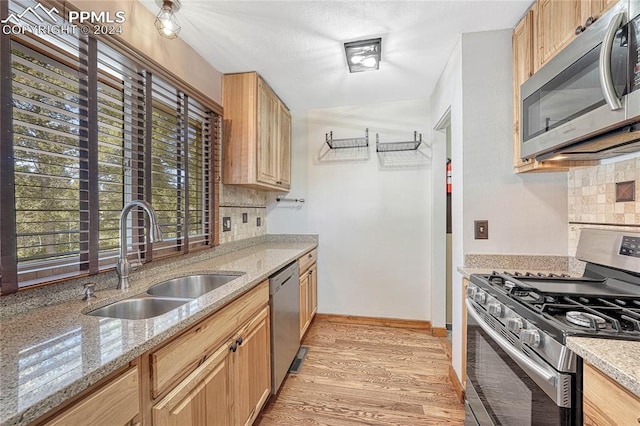 kitchen with stainless steel appliances, backsplash, sink, and light stone counters