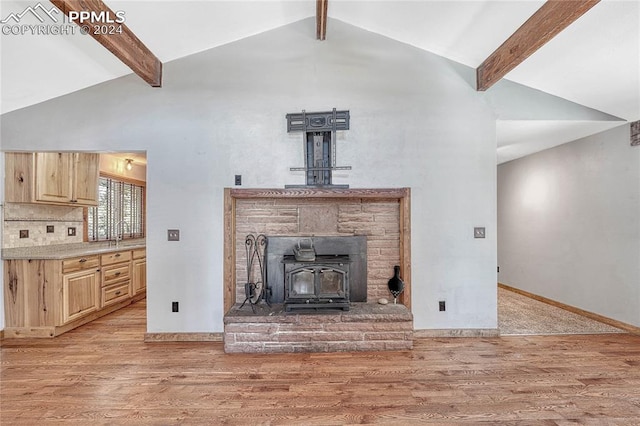 unfurnished living room featuring a wood stove, beam ceiling, and light hardwood / wood-style floors