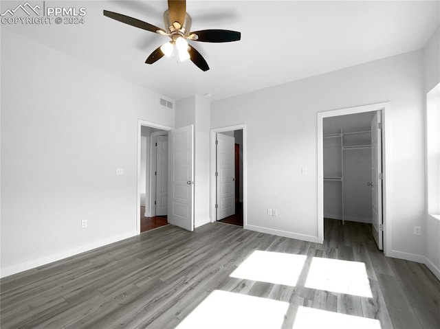 unfurnished bedroom with ceiling fan, a closet, dark hardwood / wood-style flooring, and a spacious closet