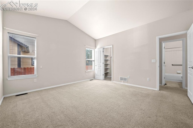 unfurnished bedroom featuring a spacious closet, vaulted ceiling, and light colored carpet