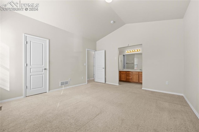 unfurnished bedroom with connected bathroom, light carpet, and vaulted ceiling