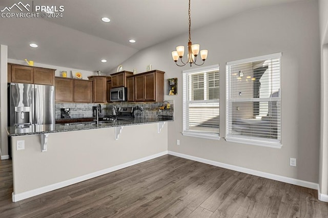 kitchen with kitchen peninsula, pendant lighting, vaulted ceiling, a breakfast bar, and appliances with stainless steel finishes