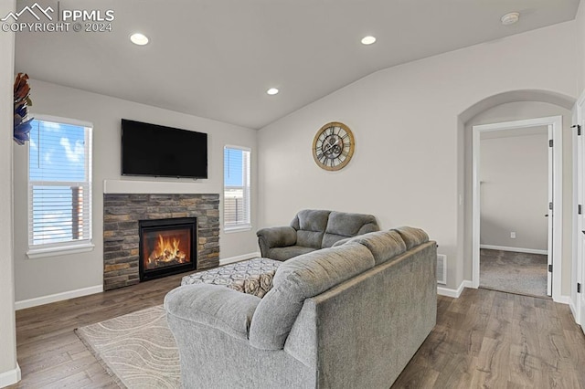 living room with a stone fireplace, a wealth of natural light, wood-type flooring, and vaulted ceiling