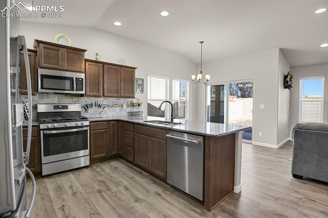 kitchen with sink, kitchen peninsula, pendant lighting, vaulted ceiling, and appliances with stainless steel finishes