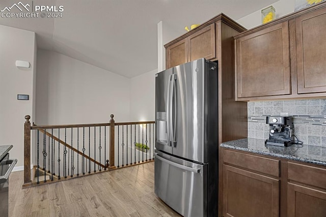 kitchen featuring stainless steel fridge with ice dispenser, backsplash, light hardwood / wood-style flooring, and dark stone countertops