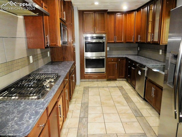 kitchen featuring stainless steel appliances, backsplash, dark stone counters, and range hood