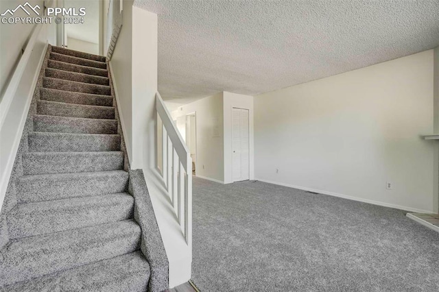 stairway featuring a textured ceiling and carpet floors