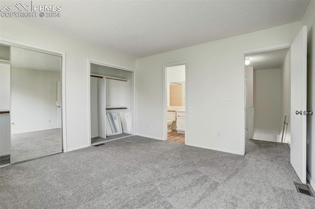 unfurnished bedroom featuring ensuite bathroom, light carpet, and a textured ceiling