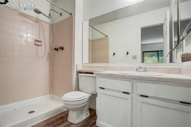 bathroom featuring vanity, tiled shower, wood-type flooring, and toilet