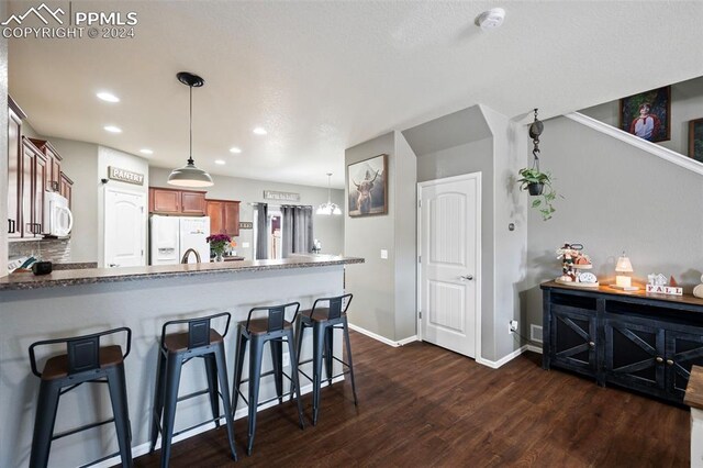 kitchen with brown cabinets, a breakfast bar area, dark wood-type flooring, white appliances, and a peninsula