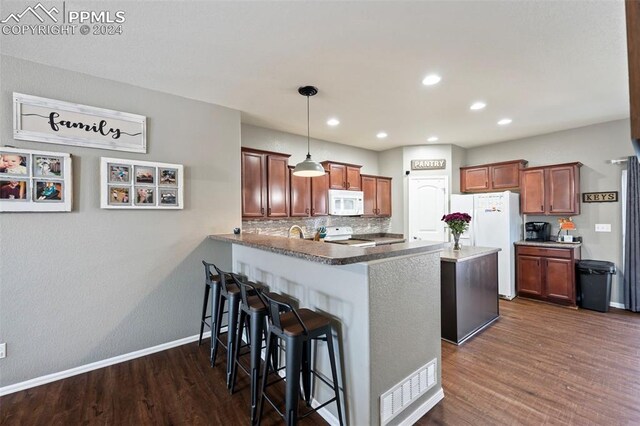 kitchen with white appliances, tasteful backsplash, dark wood-style floors, a peninsula, and a kitchen bar