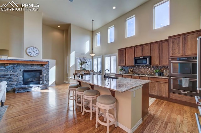 kitchen featuring decorative backsplash, a kitchen island with sink, a kitchen breakfast bar, hanging light fixtures, and black appliances