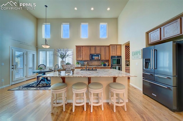 kitchen featuring tasteful backsplash, decorative light fixtures, high end refrigerator, and a center island with sink