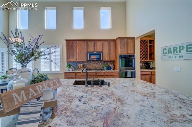 kitchen with backsplash, sink, stainless steel gas cooktop, light stone countertops, and double oven