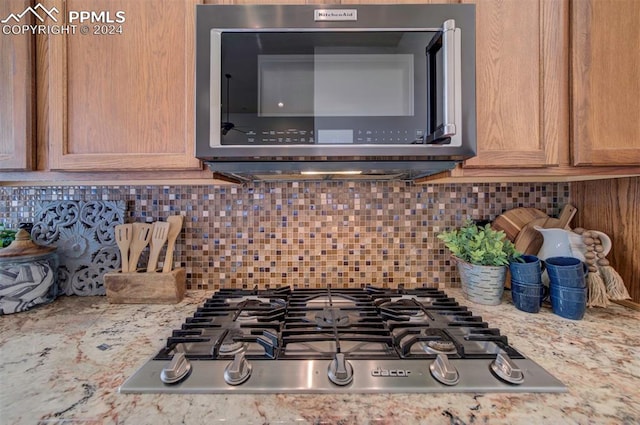 interior details featuring appliances with stainless steel finishes, decorative backsplash, and light stone counters