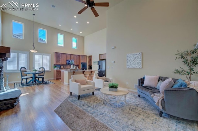 living room featuring light wood-type flooring, ceiling fan, and a high ceiling