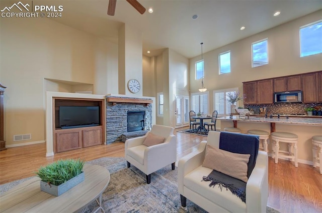 living room with ceiling fan, light wood-type flooring, a towering ceiling, and a fireplace