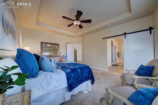 carpeted bedroom with ceiling fan, a barn door, and a tray ceiling