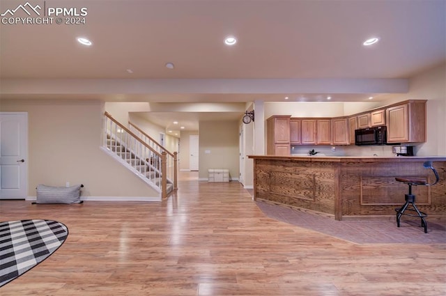 kitchen with light wood-type flooring, light brown cabinetry, kitchen peninsula, and a kitchen breakfast bar