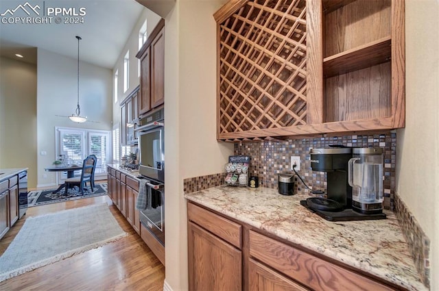 kitchen with a towering ceiling, decorative light fixtures, double oven, light stone counters, and light hardwood / wood-style flooring