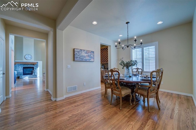 dining area with an inviting chandelier, hardwood / wood-style floors, and a stone fireplace