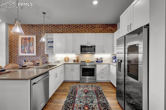 kitchen featuring stainless steel appliances, brick wall, sink, decorative light fixtures, and white cabinets