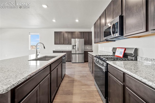 kitchen featuring light wood-type flooring, a kitchen island with sink, stainless steel appliances, sink, and dark brown cabinets