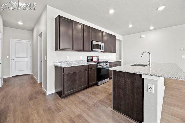 kitchen with a kitchen island with sink, light hardwood / wood-style flooring, dark brown cabinets, sink, and appliances with stainless steel finishes