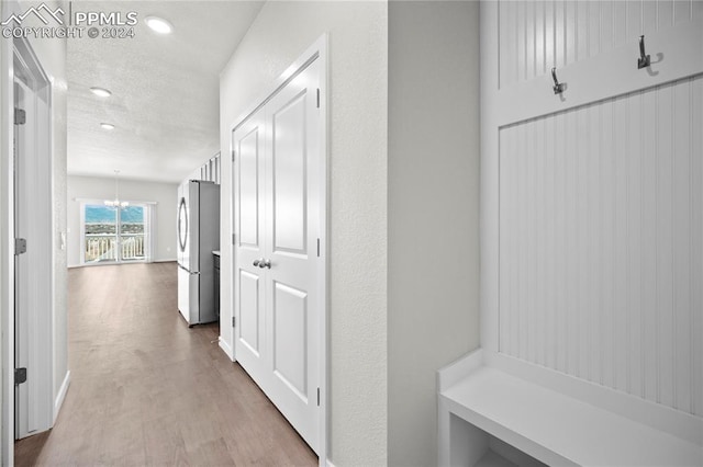 hall featuring light hardwood / wood-style floors, a notable chandelier, and a textured ceiling